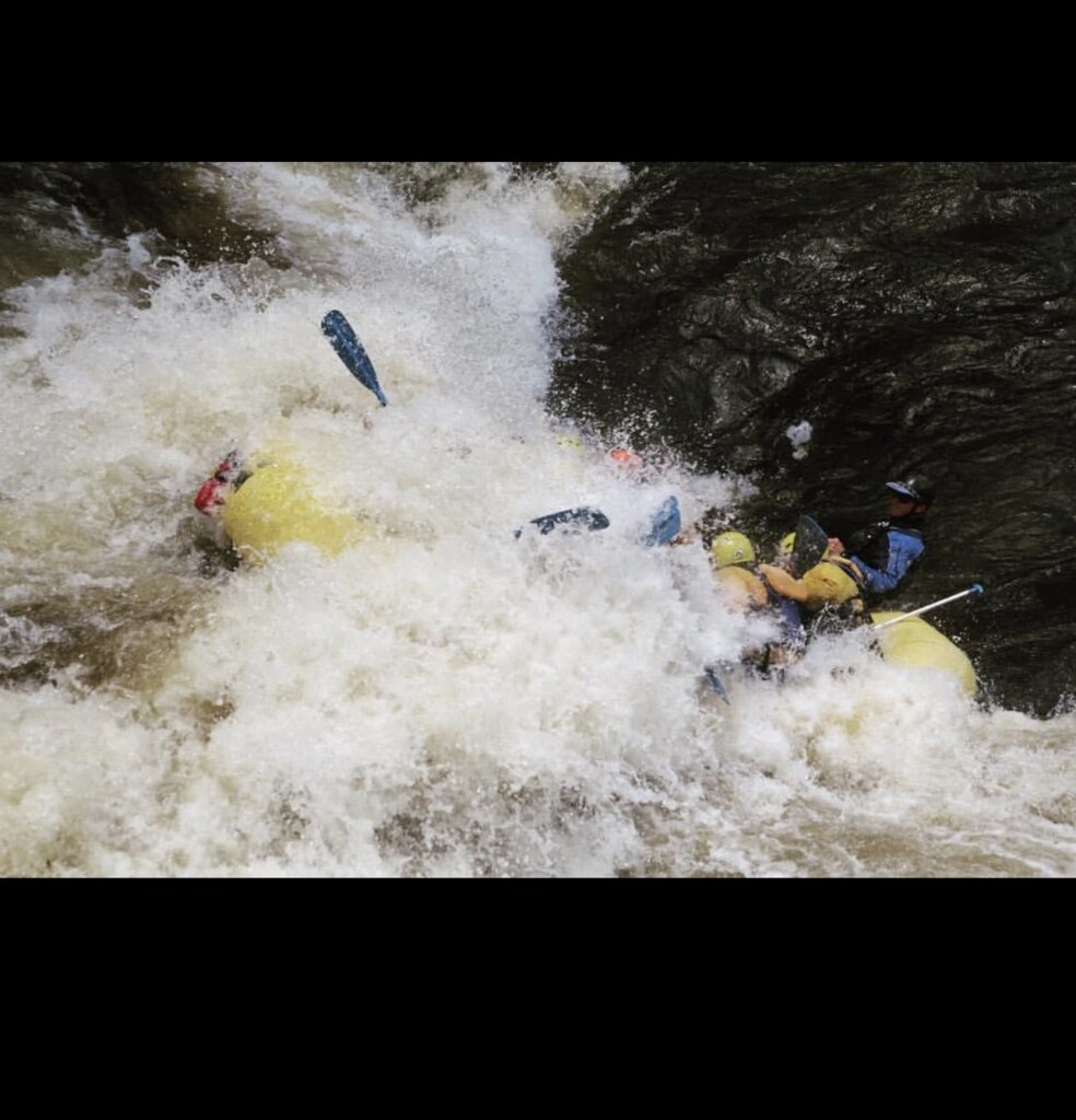 Rafters in a yellow raft surf a glassy wave into a raft swallowing hole